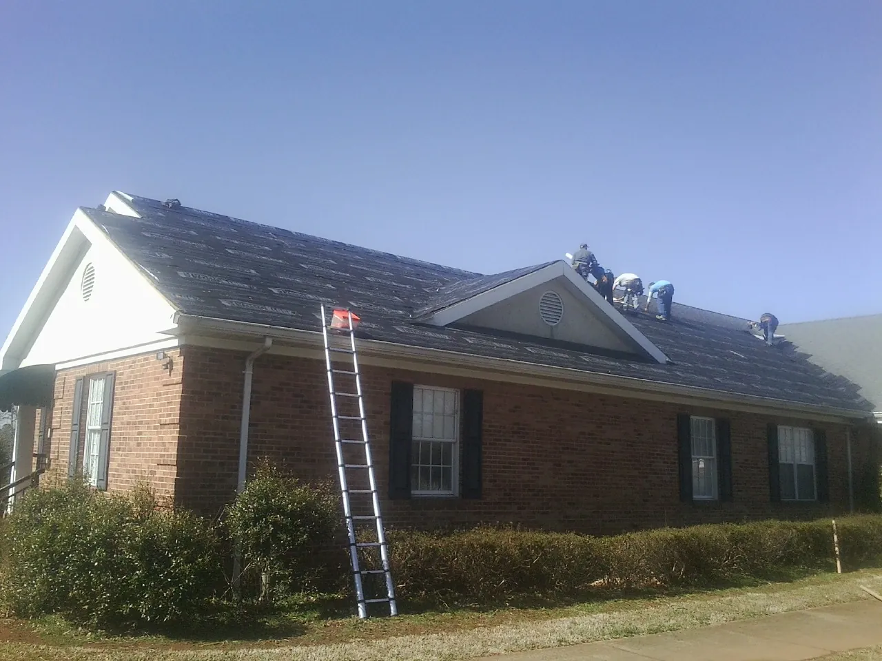 Crew tearing shingles off a brick ranch roof with a ladder set — Metal Roof Repair work by our crew in Timmonsville