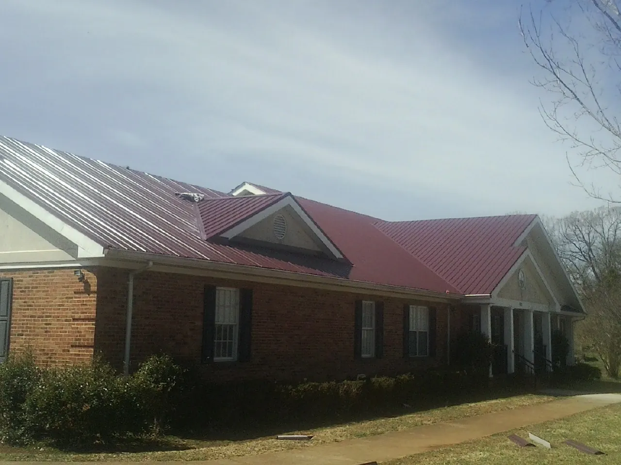 Red metal roof with gabled entries on a long brick building, from a Hail Damage Roof Repair job in Timmonsville