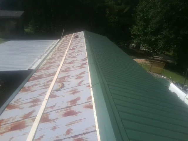 Old rusted panels beside newly installed green metal roofing — Wind Damage Roof Repair by Roofing Brothers in Timmonsville