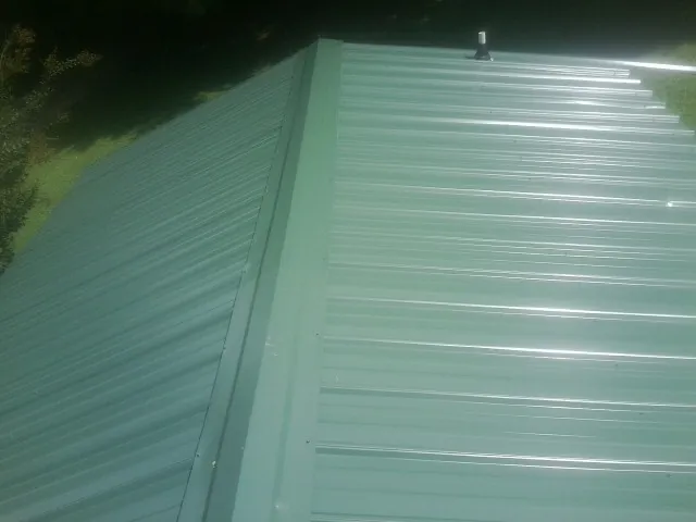 New green metal panels meeting at the ridge of a roof — Flat Roof Repair work by our crew in Timmonsville