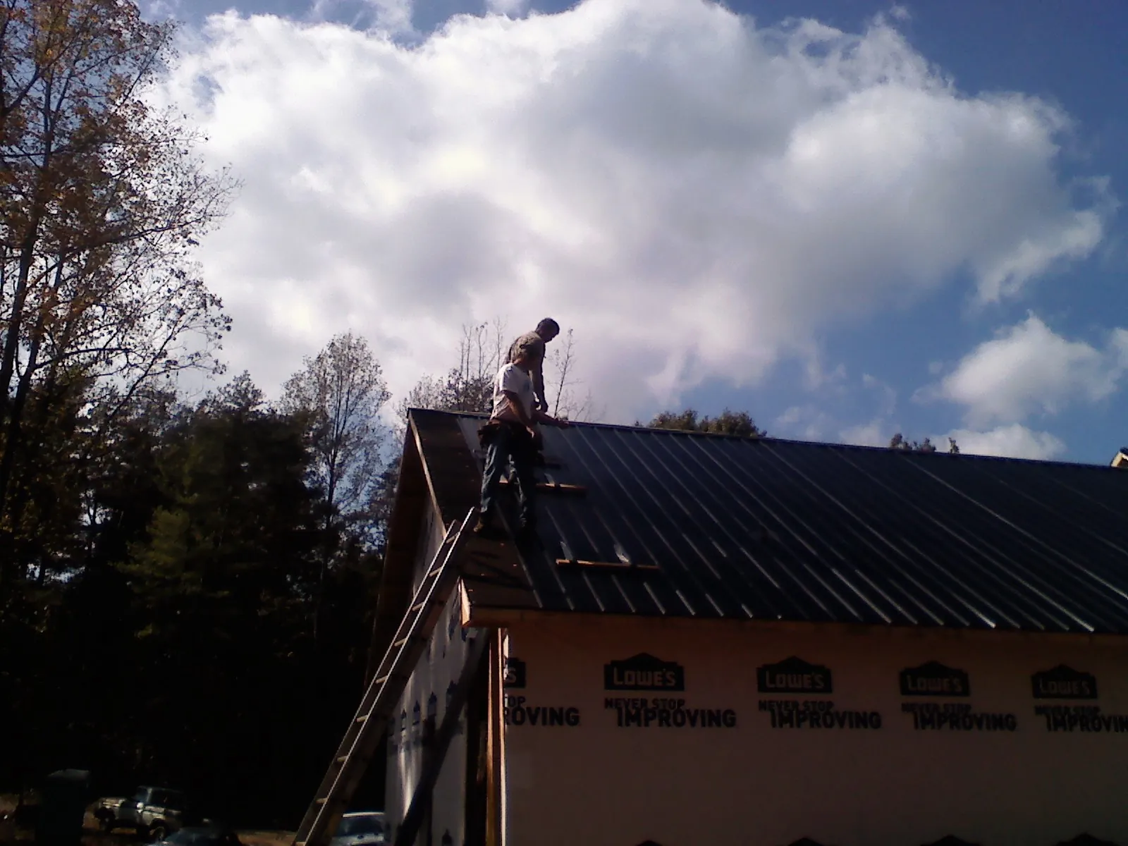 Roofer fastening dark metal panels high against a cloudy sky, from a Roof Inspection job in Timmonsville