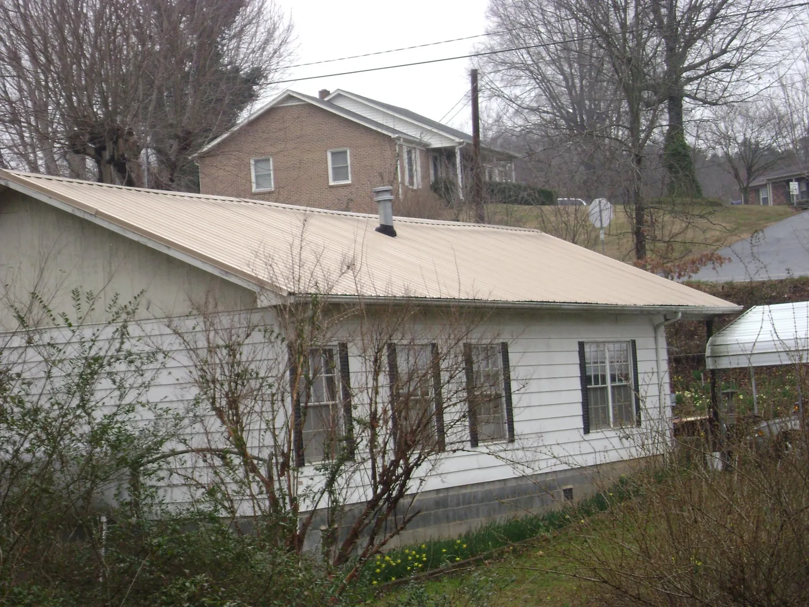 Tan metal roof on a white sided house set into a hillside — Commercial Roofing by Roofing Brothers in Timmonsville
